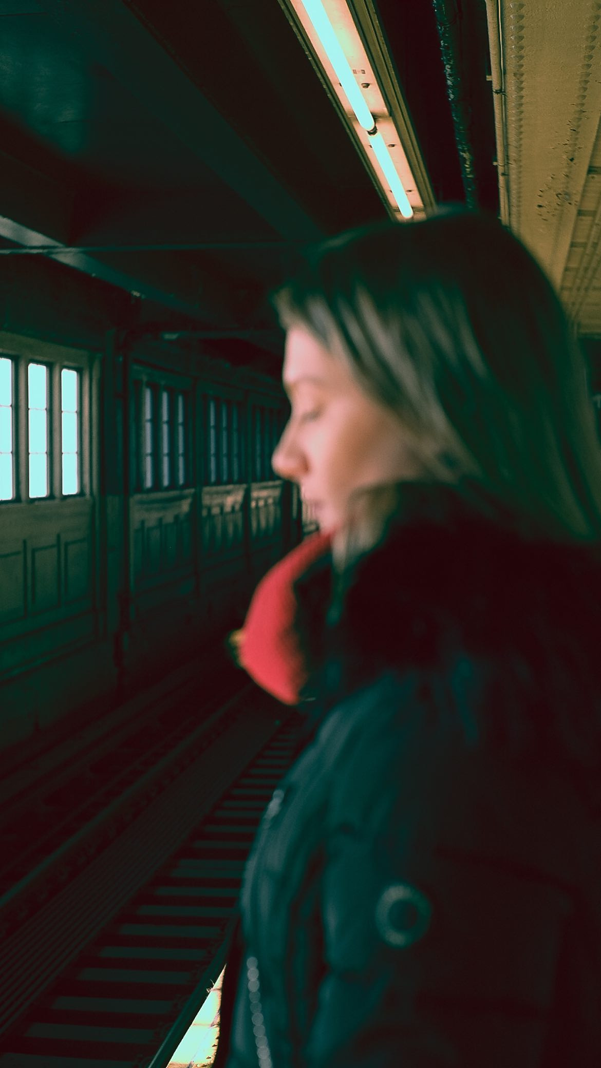 Woman in profile in a fur-collared coat, green neon light of a station