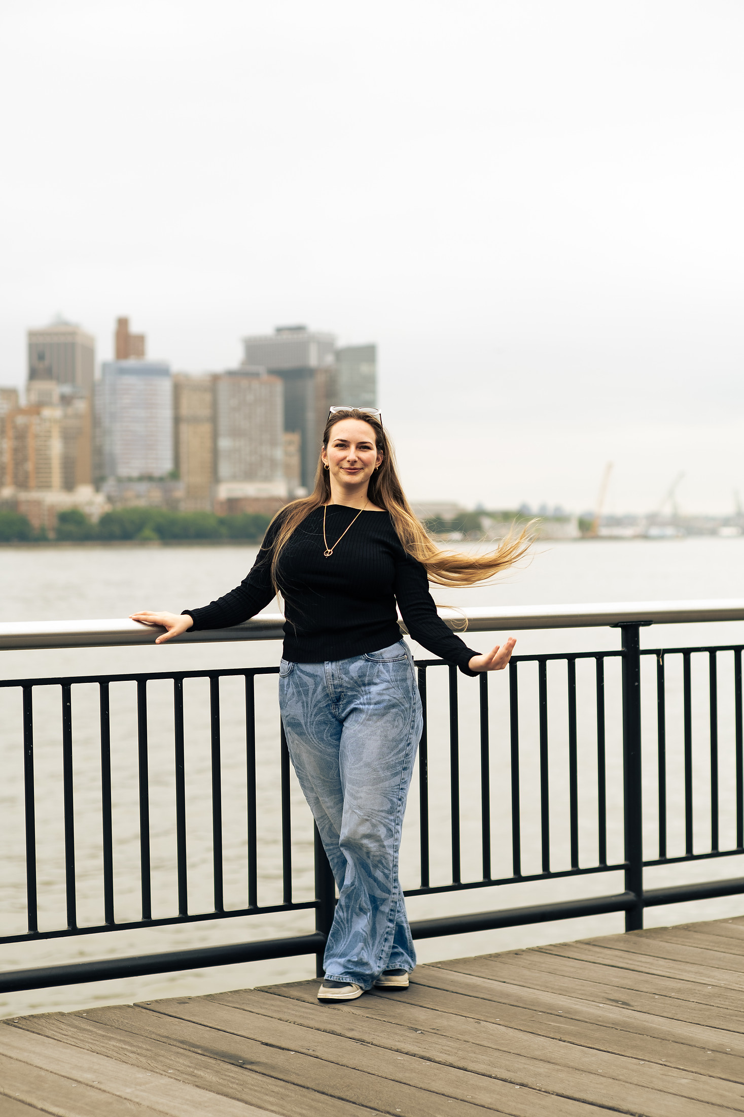Woman laughing on a pier with the New York skyline behind her