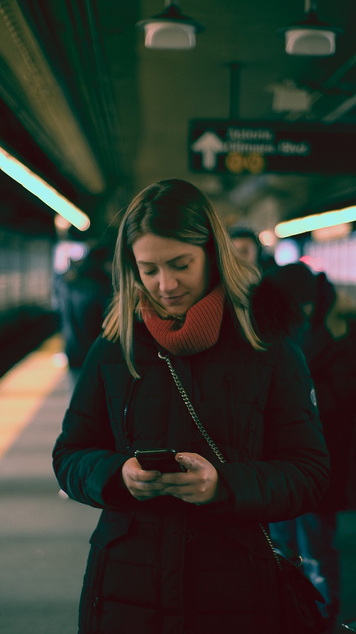 Woman in a red coat looking at her phone on the subway