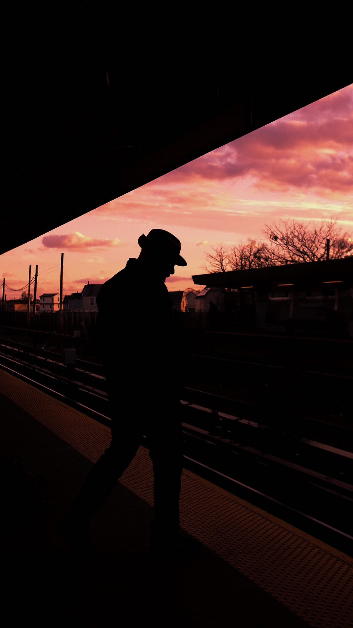 Silhouette of a man on a train platform against a pink sunset