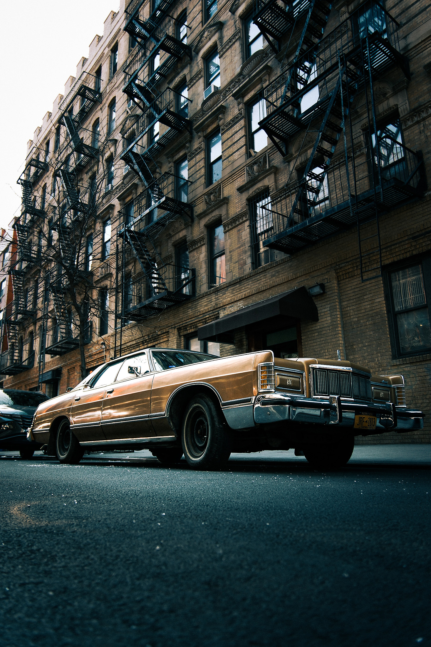 Gold classic car parked in front of a building with fire escapes
