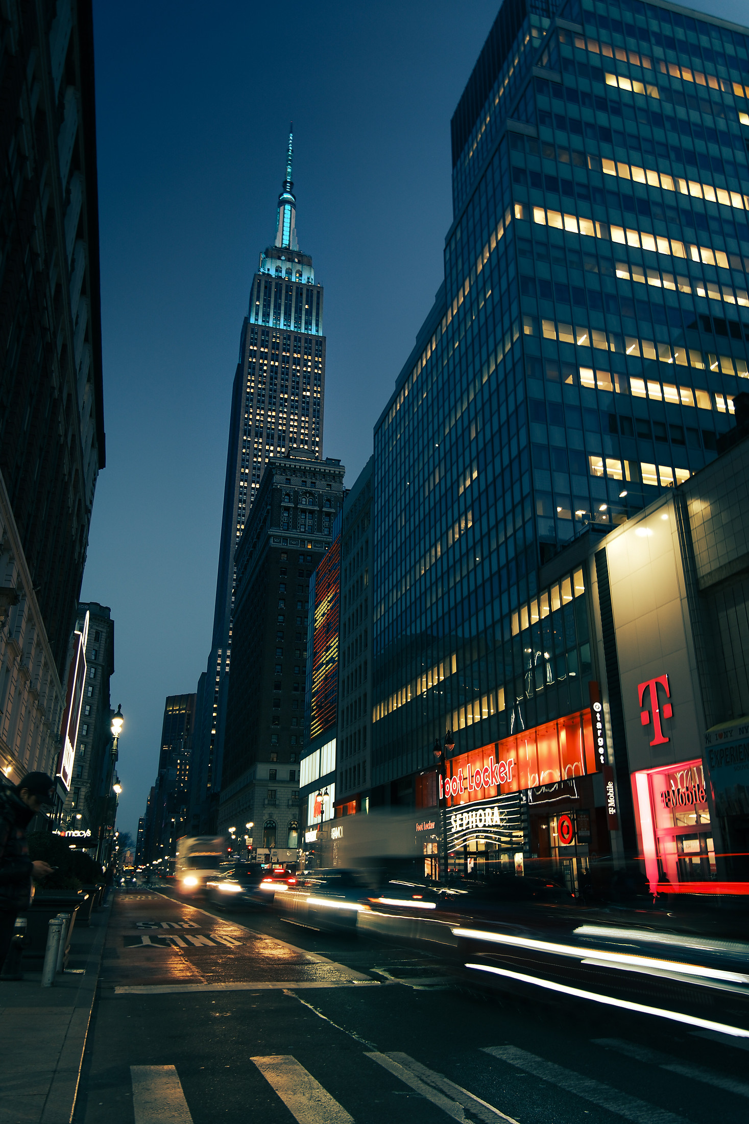 The Empire State Building at night, light trails along the avenue