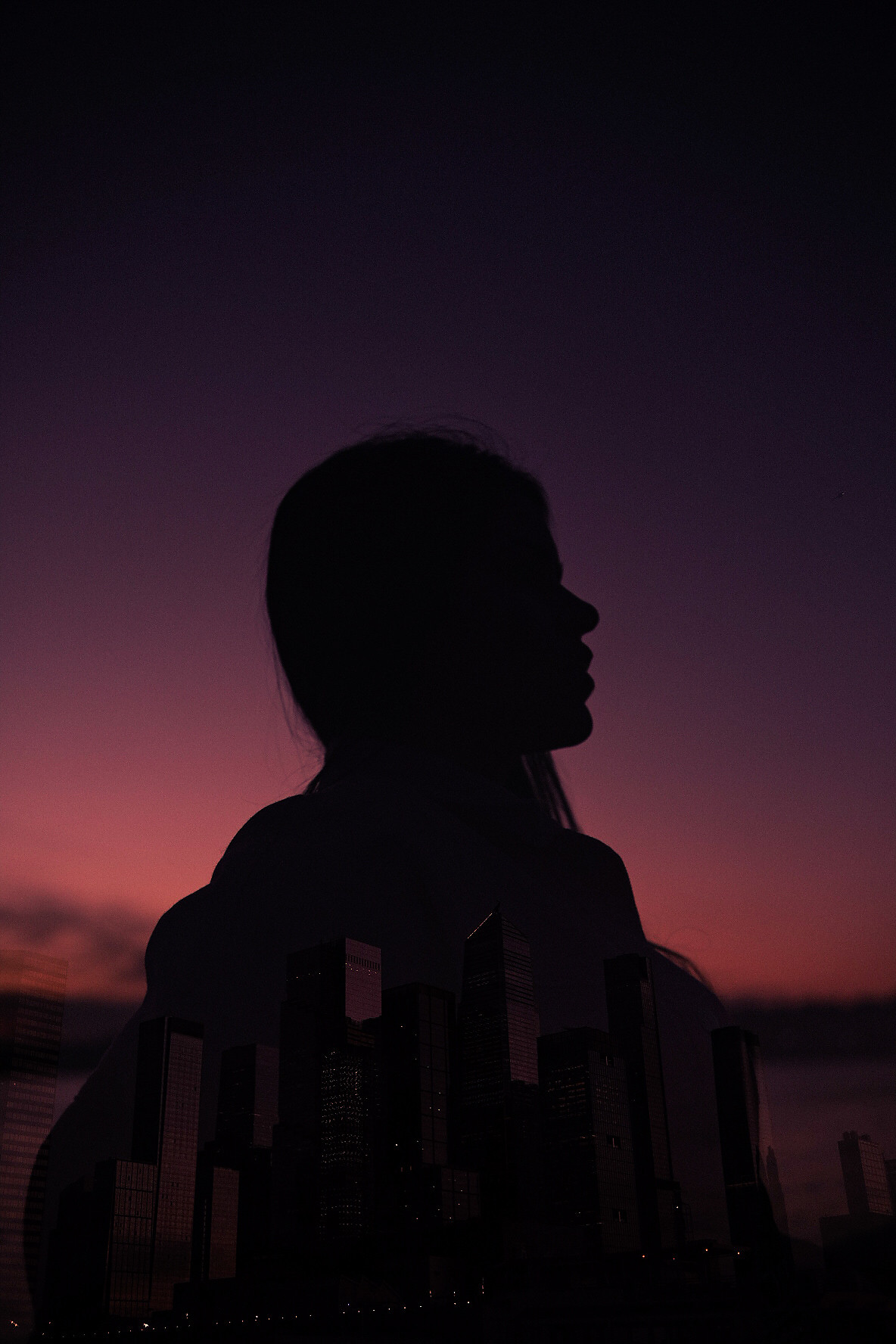 Double exposure: a silhouetted profile with the city inside it against a violet sky